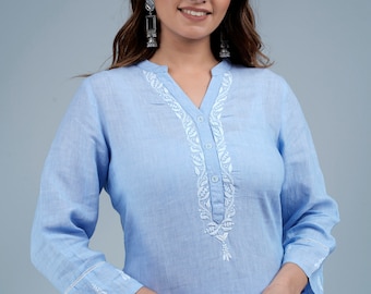 May include: A light blue linen tunic top with white embroidery. The embroidery features a floral design with a tassel at the bottom. The top has a V-neck and three-quarter sleeves.