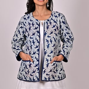 May include: A blue and white quilted jacket with a bird print and a zip closure. The jacket has two pockets and a white trim.
