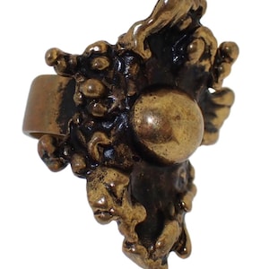 May include: A large, abstract, bronze ring with a textured, organic design. The ring has a large, round, smooth, bronze bead in the center.