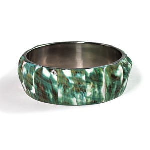 Può includere: Un bracciale rigido largo caratterizzato da un esterno segmentato con un motivo marmorizzato nei toni del verde bosco profondo, bianco e marrone scuro. L'interno della fascia circolare è rifinito in una tonalità argento metallizzato liscio.
