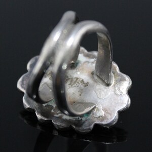 May include: Silver ring with a turquoise stone set in a floral design. The ring has a wide band and a simple, elegant design.