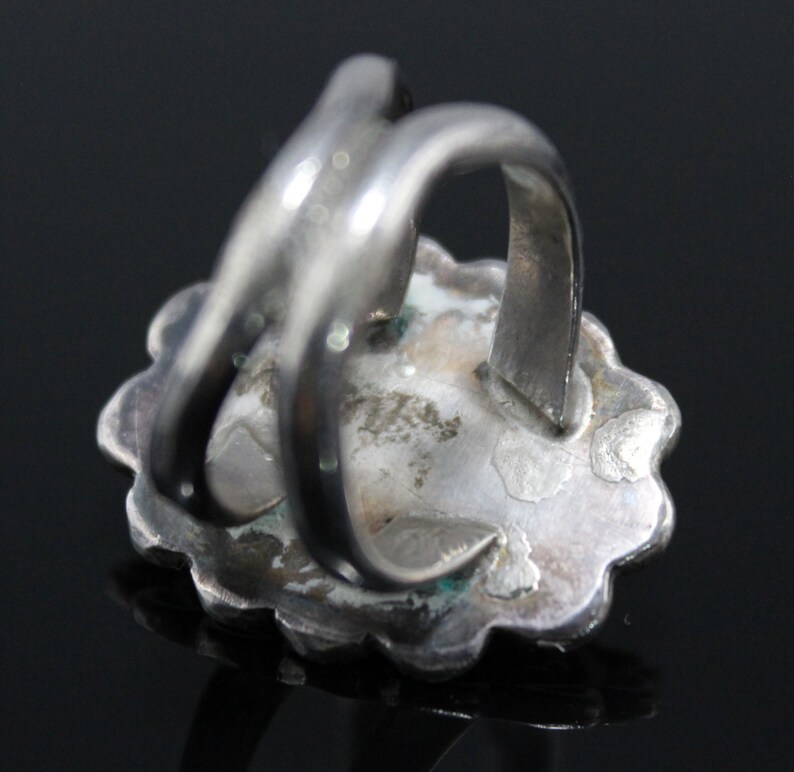 May include: Silver ring with a turquoise stone set in a floral design. The ring has a wide band and a simple, elegant design.