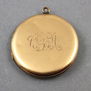 May include: A gold locket with a hinged lid and a loop for a chain. The locket has an engraved monogram of the letters "E.E.H."