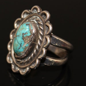 May include: A silver ring with a turquoise stone set in a detailed, scalloped design. The ring has a double band.