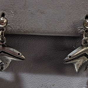 Puede incluir: Un par de pendientes de plata con un diseño de oso. El oso está estilizado con un patrón de zigzag y un diseño de sol en la parte posterior.
