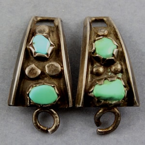 May include: A pair of silver and turquoise concho belt buckles. Each buckle has three turquoise stones and a silver loop on the bottom.