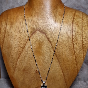 May include: A silver chain necklace with a square pendant featuring a black and silver geometric design.