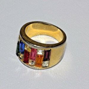 May include: A gold ring with a band of colorful rectangular stones. The stones are set in a silver band and are arranged in a row. The ring is a statement piece and would be a great addition to any jewelry collection.