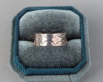 Könnte beinhalten: Ein silberner Ring mit geometrischem Muster. Der Ring befindet sich in einer blauen Samt-Ringbox.