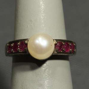 May include: A silver ring with a large white pearl and a band of small red rubies.