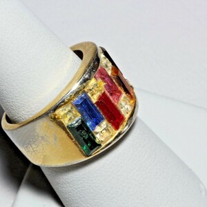 May include: A gold ring with a band of colorful gemstones. The stones are set in a row and include red, pink, blue, green, and yellow.