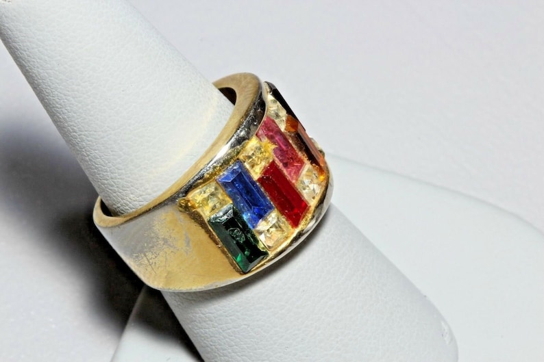 May include: A gold ring with a band of colorful gemstones. The stones are set in a row and include red, pink, blue, green, and yellow.