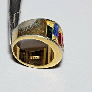 May include: A gold band ring with a multi-colored enamel design. The enamel is in shades of red, green, blue, and gold. The ring is set with small red stones.