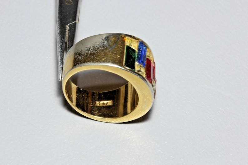 May include: A gold band ring with a multi-colored enamel design. The enamel is in shades of red, green, blue, and gold. The ring is set with small red stones.