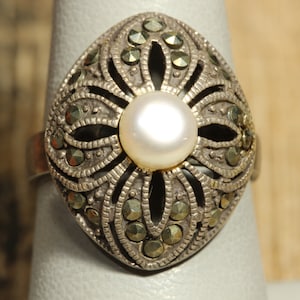 May include: A silver ring featuring a pearl centre stone and a floral design set with marcasite stones.