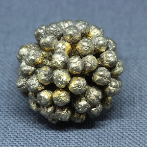 May include: A cluster of small, metallic, silver and gold spheres, resembling a miniature, textured ball.