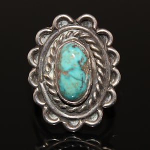 May include: A silver ring with a turquoise stone set in a detailed, scalloped design.