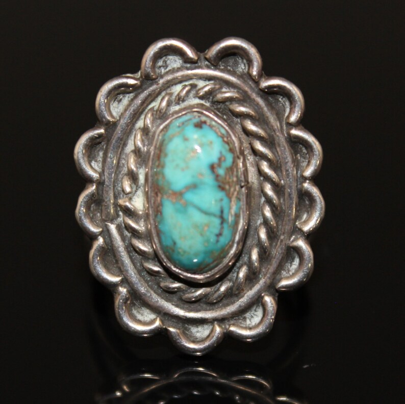 May include: A silver ring with a turquoise stone set in a detailed, scalloped design.