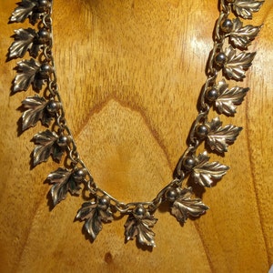 May include: A gold-toned necklace with a chain and leaf-shaped pendants. The necklace is displayed on a wooden mannequin.