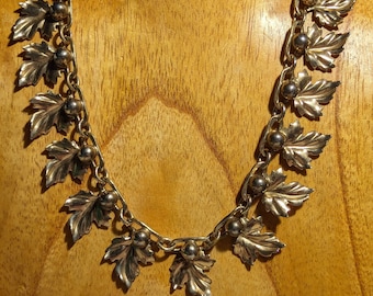 May include: A gold-toned necklace with a chain and leaf-shaped pendants. The necklace is displayed on a wooden mannequin.