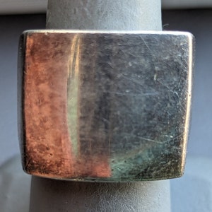 May include: A silver square ring with a smooth, slightly textured surface. The ring has a rounded edge and a polished finish.