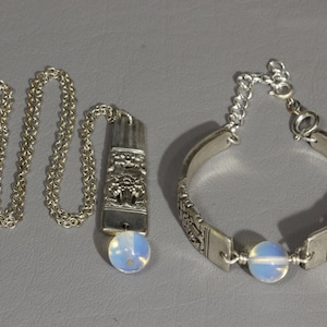 Puede incluir: Un collar de plata con un colgante y una pulsera de plata con dos cuentas de ópalo. Ambas piezas presentan intrincados diseños florales.