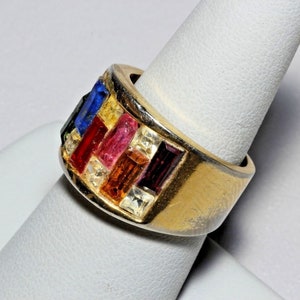 May include: A gold ring with a wide band set with colorful rectangular stones. The stones are arranged in a geometric pattern and include red, pink, yellow, blue, and clear stones.