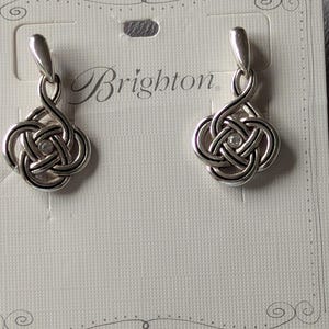 May include: A pair of silver-toned Brighton earrings. Each earring features a Celtic knot design with a small, clear crystal in the center. The earrings are displayed on a white card with the Brighton logo.