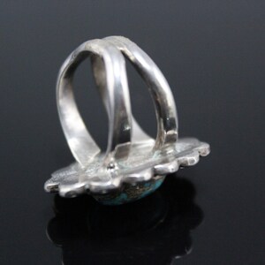 May include: A silver ring with a turquoise stone set in a floral design. The ring is double-banded and has a wide, flat band.