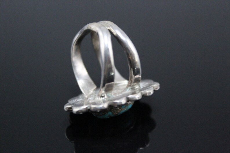 May include: A silver ring with a turquoise stone set in a floral design. The ring is double-banded and has a wide, flat band.