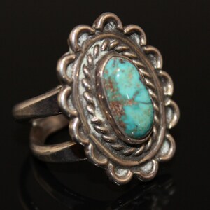 May include: A silver ring with a turquoise stone set in a detailed silver design. The ring has a double band.