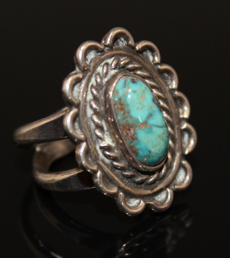 May include: A silver ring with a turquoise stone set in a detailed silver design. The ring has a double band.