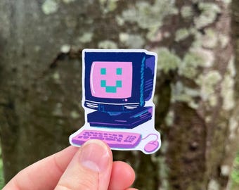 May include: A sticker of a retro computer with a pink screen displaying a smiling face. The keyboard and mouse are also pink. The computer is dark blue with purple accents.