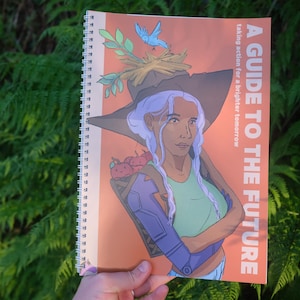 May include: A spiral-bound notebook with the title "A Guide to the Future" on the cover. The illustration features a woman with a witch hat, a blue bird, and a basket of red fruit. The background is orange.