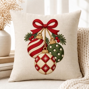 Peut inclure: Un coussin carr&eacute; blanc cass&eacute; orn&eacute; d'une broderie repr&eacute;sentant trois boules de No&euml;l suspendues dans des tons rouge, vert et cr&egrave;me. Les boules sont nou&eacute;es par un ruban rouge, agr&eacute;ment&eacute;es de branches de pin vertes et de petites baies rouges.