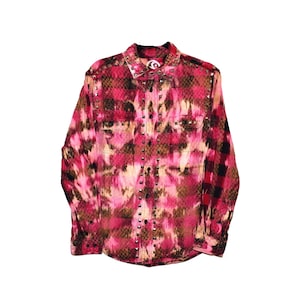 May include: A button-down shirt with a pink, brown, and black tie-dye pattern. The shirt has a collared neckline, two chest pockets, and metal stud accents along the placket and cuffs. The fabric appears to be a blend of cotton and possibly silk.