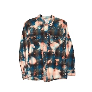 May include: A long-sleeved button-down shirt with a unique tie-dye pattern in shades of blue, brown, and peach. The shirt features silver stud accents along the seams and collar, and has two chest pockets. The shirt is a western style.