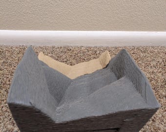 May include: A grey and brown cardboard box with a textured surface. The box is folded in half and has a rectangular shape.