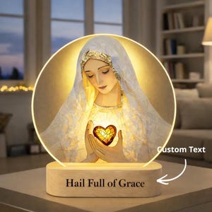 May include: A religious-themed LED lamp featuring an image of a saint holding a heart. The lamp has a wooden base with the text "Hail Full of Grace". The image is illuminated by a warm, soft light.