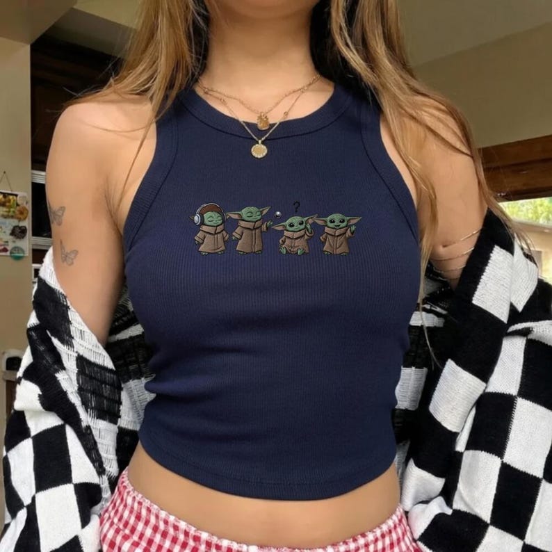 May include: Navy blue ribbed tank top featuring an embroidered design of four Grogu characters. The characters are in various poses, with one wearing headphones and another with a question mark above its head. The top has a round neckline and a sleeveless design.