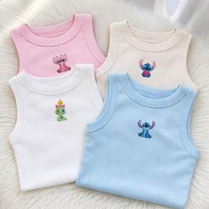 May include: Four sleeveless tank tops in pastel colors: pink, cream, white, and light blue. Each top features an embroidered cartoon character. The tops are made of a soft, ribbed fabric, perfect for warm weather or layering.