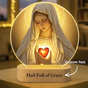 May include: A religious-themed night light featuring an image of a woman holding a glowing heart. The image is set within a circular frame and rests on a wooden base with the text "Hail Full of Grace".