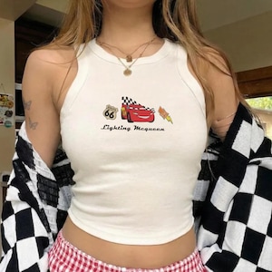 May include: White tank top with a graphic of Lightning McQueen from the Cars movie, Route 66 logo, and text "Lightning McQueen". The top is sleeveless and has a round neckline.