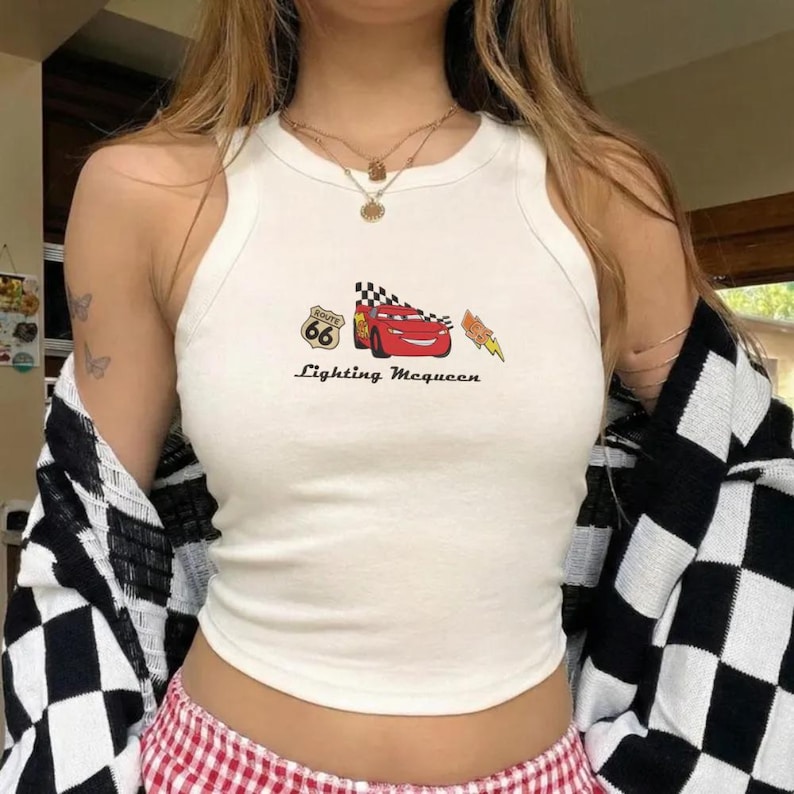 May include: White tank top with a graphic of Lightning McQueen from the Cars movie, Route 66 logo, and text "Lightning McQueen". The top is sleeveless and has a round neckline.