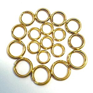 Peut inclure: Un assortiment de anneaux de jonction dorés de différentes tailles, disposés sur une surface blanche. Les anneaux circulaires semblent être en métal et ont une finition brillante. Ces anneaux sont utilisés en bijouterie et artisanat.