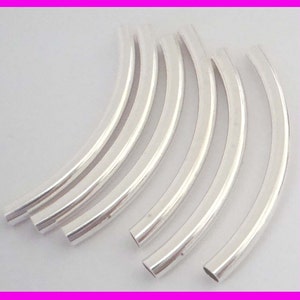 May include: A collection of six curved, silver-colored metal tubes. Each tube has a smooth, reflective surface and a rounded shape. The tubes are arranged in a parallel, slightly overlapping pattern against a light background.