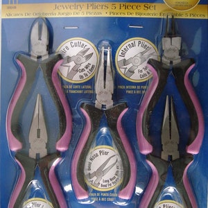 May include: A five-piece jewelry pliers set by Darice. The set includes various pliers with black and pink handles. The packaging features the text "Jewelry Designer" and "Comfort Grip Handles."