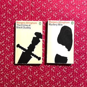 Puede incluir: Dos libros de bolsillo vintage de Margery Allingham. Las portadas son de color crema con ilustraciones en negro. Uno presenta una espada, el otro una silueta. Los títulos incluyen "The Crime at Black Dudley" y "Mystery Mile."