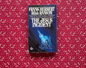 May include: A vintage paperback book titled "THE JESUS INCIDENT" by Frank Herbert and Bill Ransom. The cover features a blue and black illustration of a spacecraft. The book is set against a red floral patterned background.
