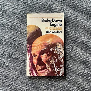 May include: A vintage paperback book titled "Broke Down Engine" by Ron Goulart. The cover features a portrait of a man and a depiction of machinery. The book is set against a gray textured background.